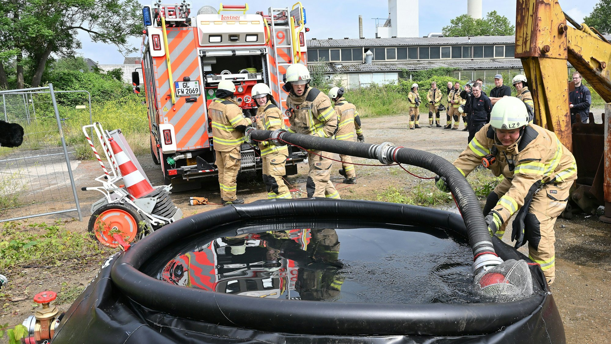 Feuerwehrleute legen eine Saugleitung von einem Feuerwehrfahrzeug in ein großes Wasserbassin.