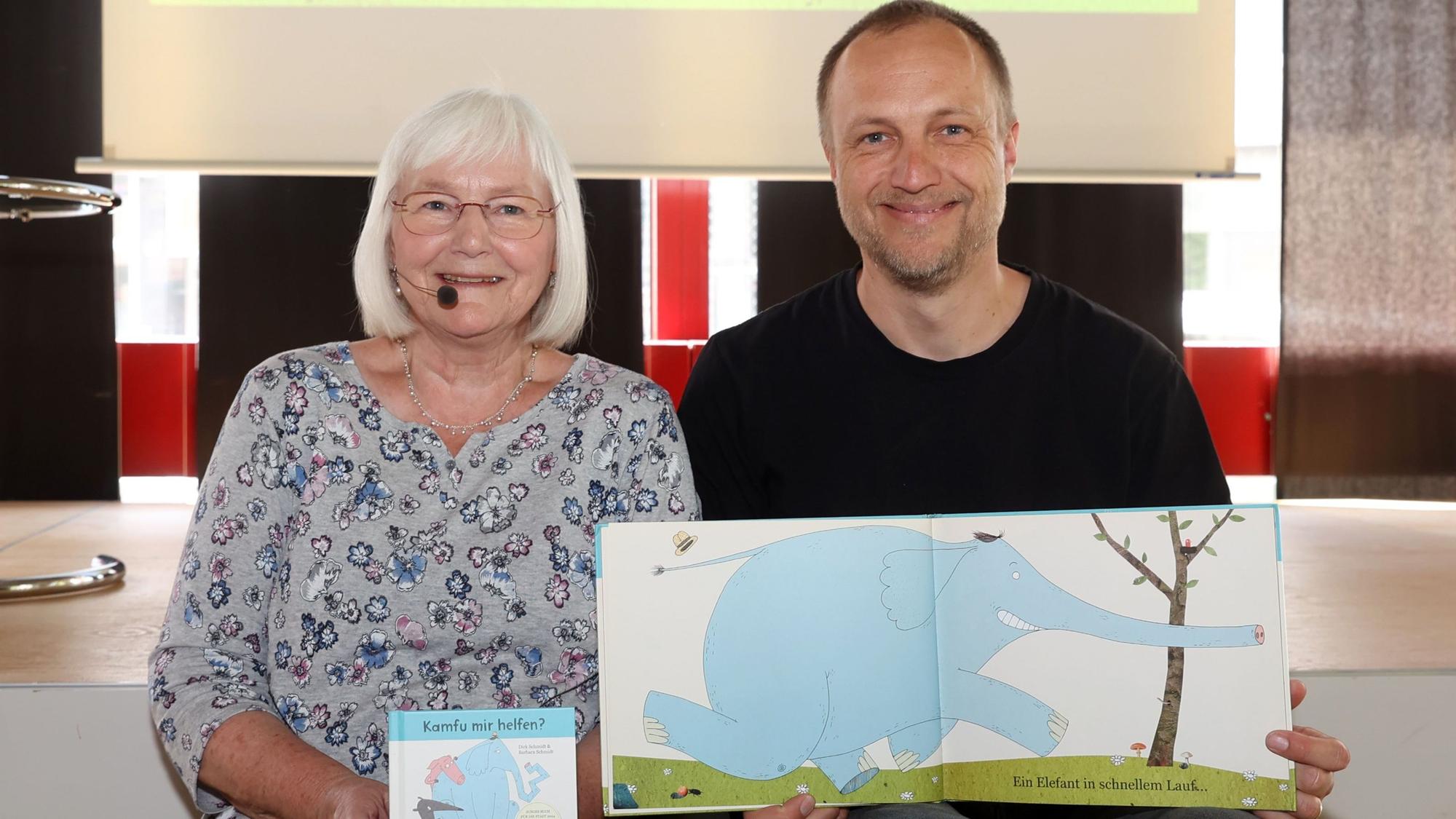 Barbara und Dirk Schmidt sitzen auf der Bühne der Stadtbibliothek. Er hält eine Zeichnung aus dem Buch „Kamfu mir helfen?“ ins Bild.