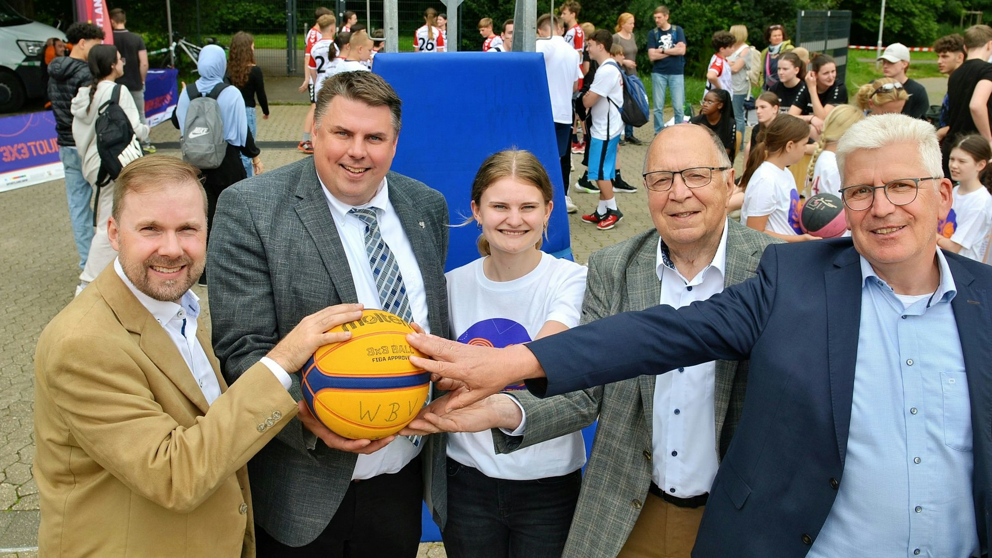 Sven Reichert, Michael Mombaur, Lexi Kitz, stellvertretender Landrat Leo Wolter und 1. Beigeordneter der Stadt Alfred Jaax halten zusammen einen orange-blauen Basketball in den Händen.