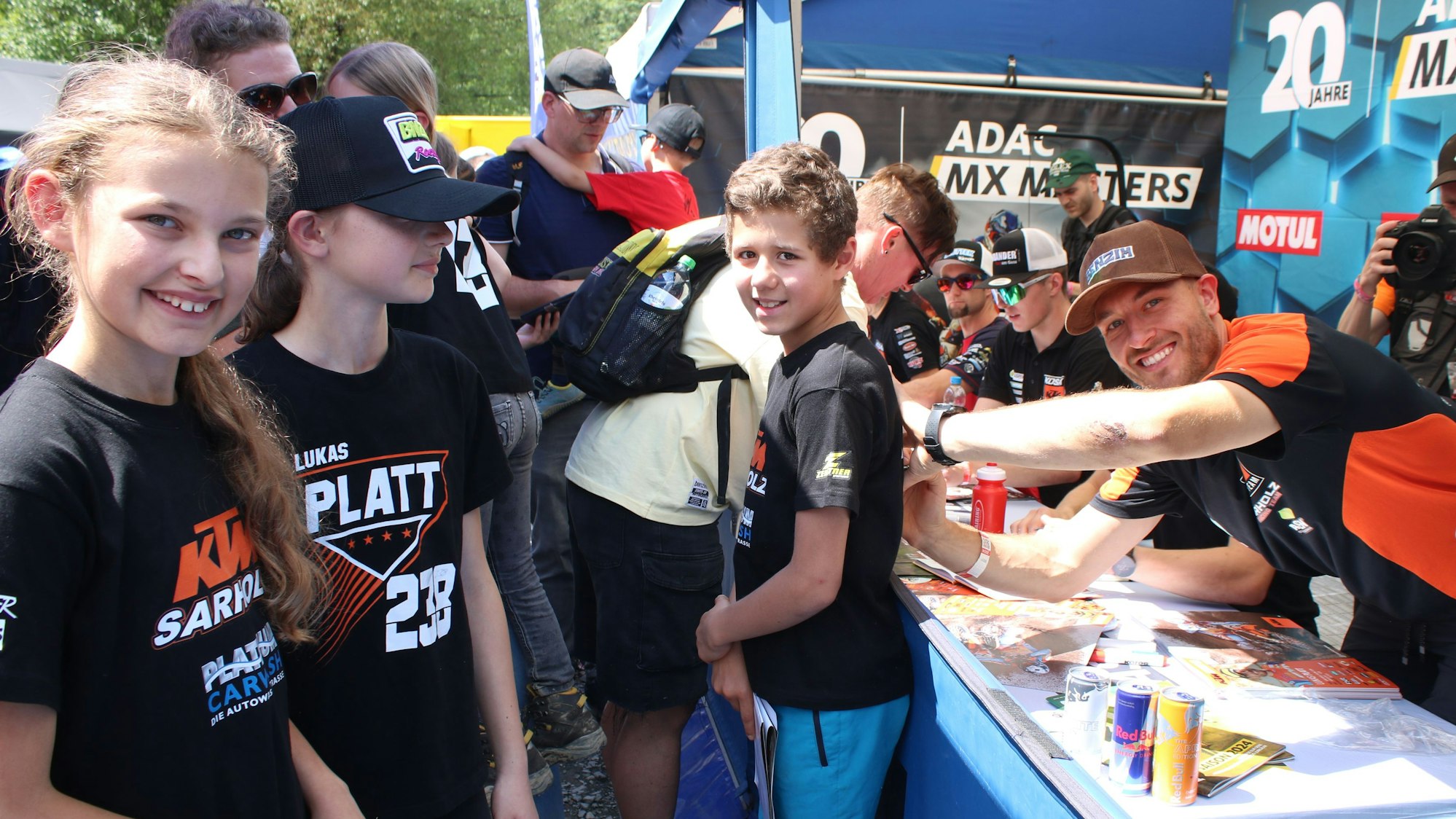 Motocrosser Lukas Platt lacht in die Kamera während er ein T-Shirt signiert.