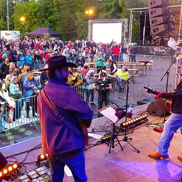 Männer in Cowboy-Hüten stehen auf einer Bühne und spielen Gitarre. Vor der Bühne haben sich zahlreiche Menschen versammelt.