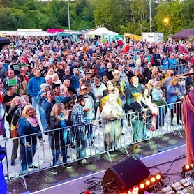 Männer in Cowboy-Hüten stehen auf einer Bühne und spielen Gitarre. Vor der Bühne haben sich zahlreiche Menschen versammelt.