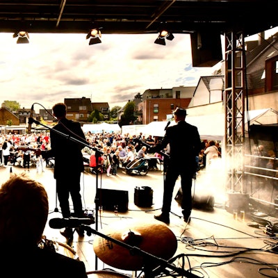 Zu sehen sind eine Band auf einer Bühne und im Hintergrund die Zuschauer.