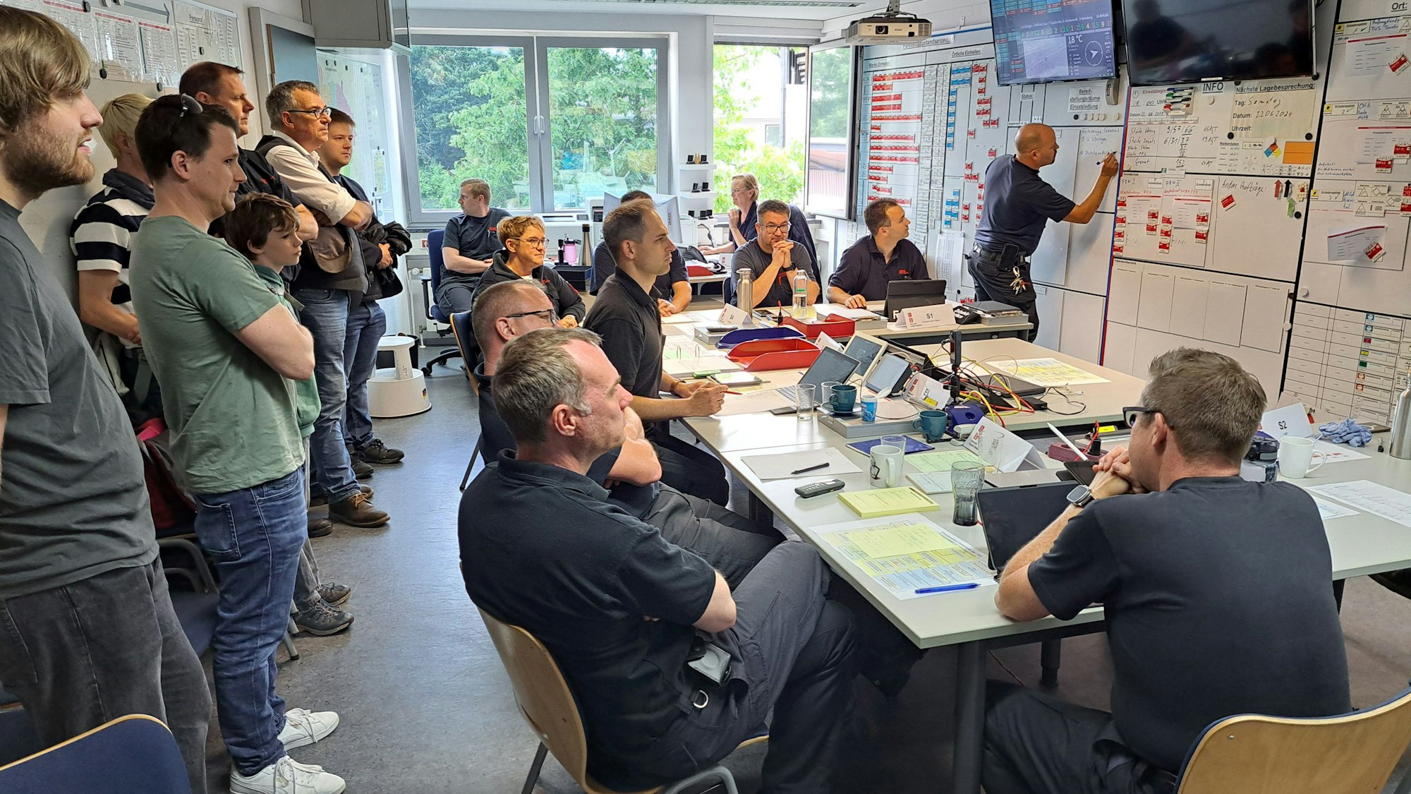 Menschen schauen der Arbeit des Stabs in der Feuerwehr-Einsatz-Leitstelle über die Schulter.