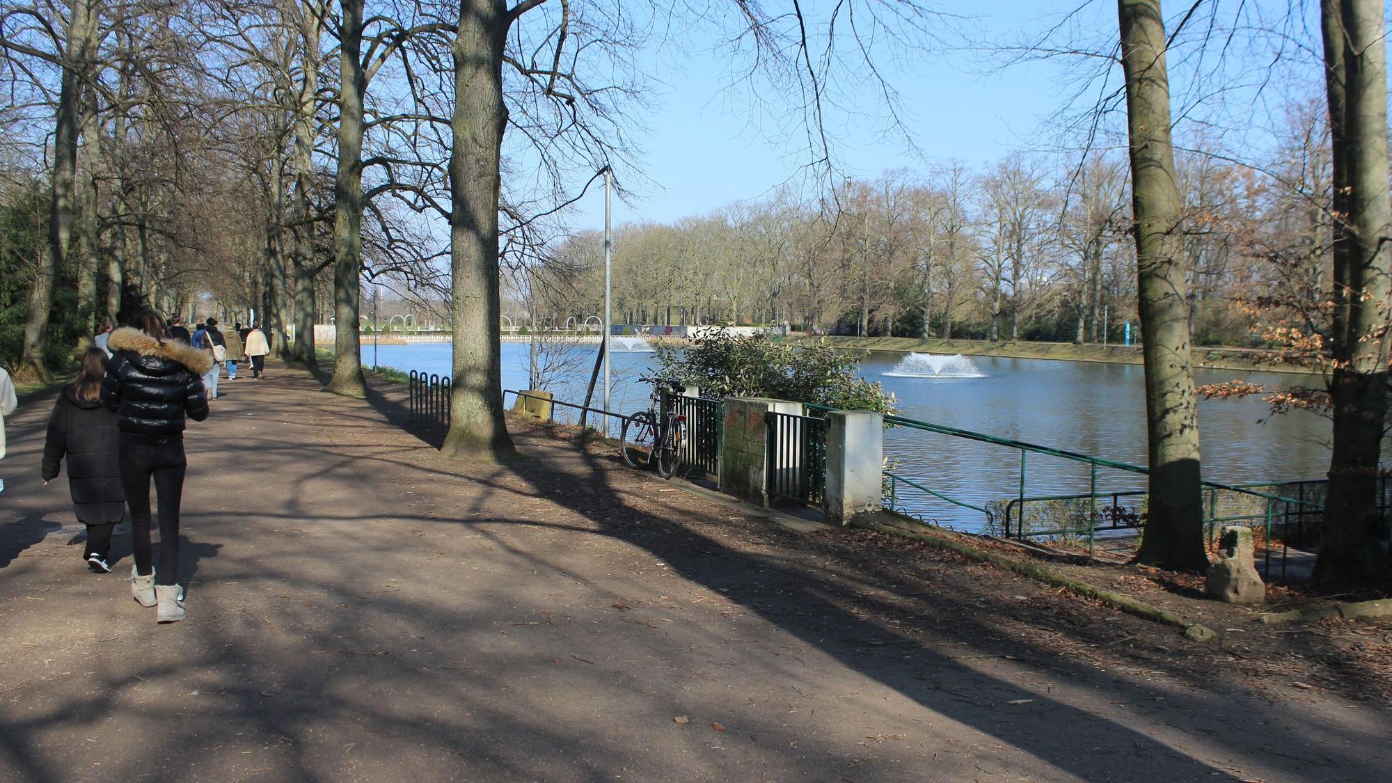 Zu sehen ist ein Park mit einem Gewässer und ein paar Menschen.