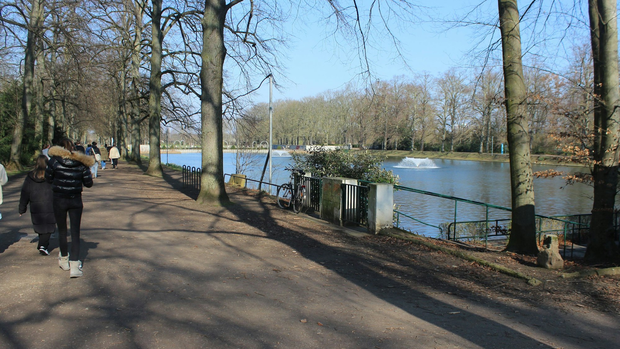 Zu sehen ist ein Park mit einem Gewässer und ein paar Menschen.