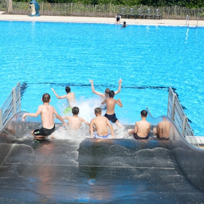 Jungen rutschen eine breite Wasserrutsche herunter.