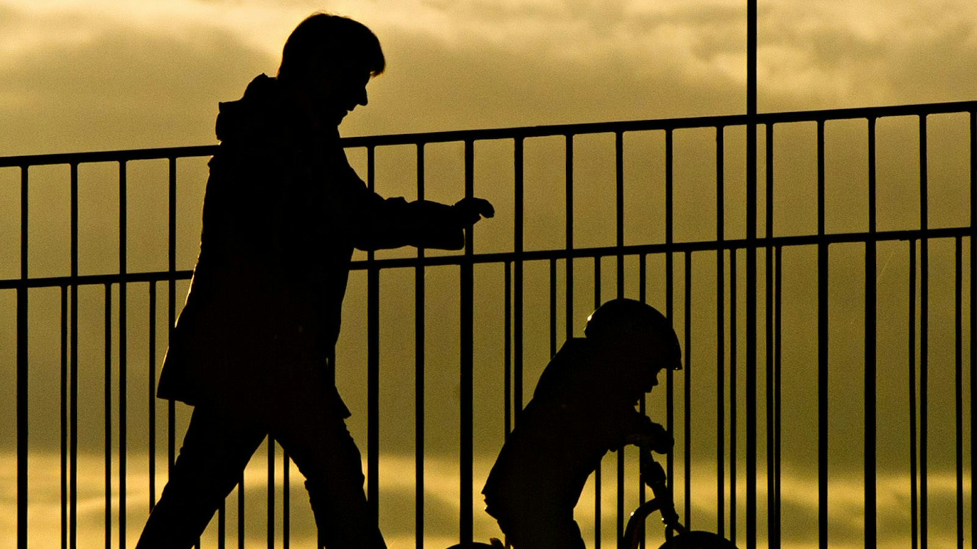 Eine Frau geht mit einem Kind bei Sonnenaufgang über eine Brücke.