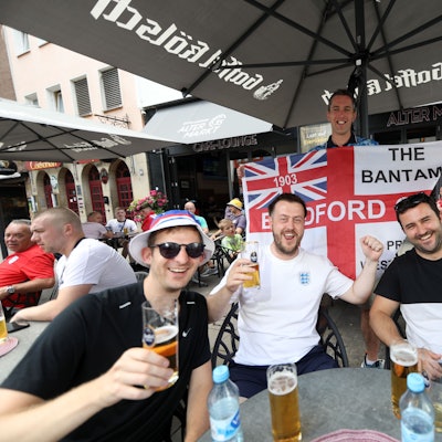 Englandfans sitzen am Alter Markt in einem Restaurant und prosten mit einem Glas Bier in die Kamera.