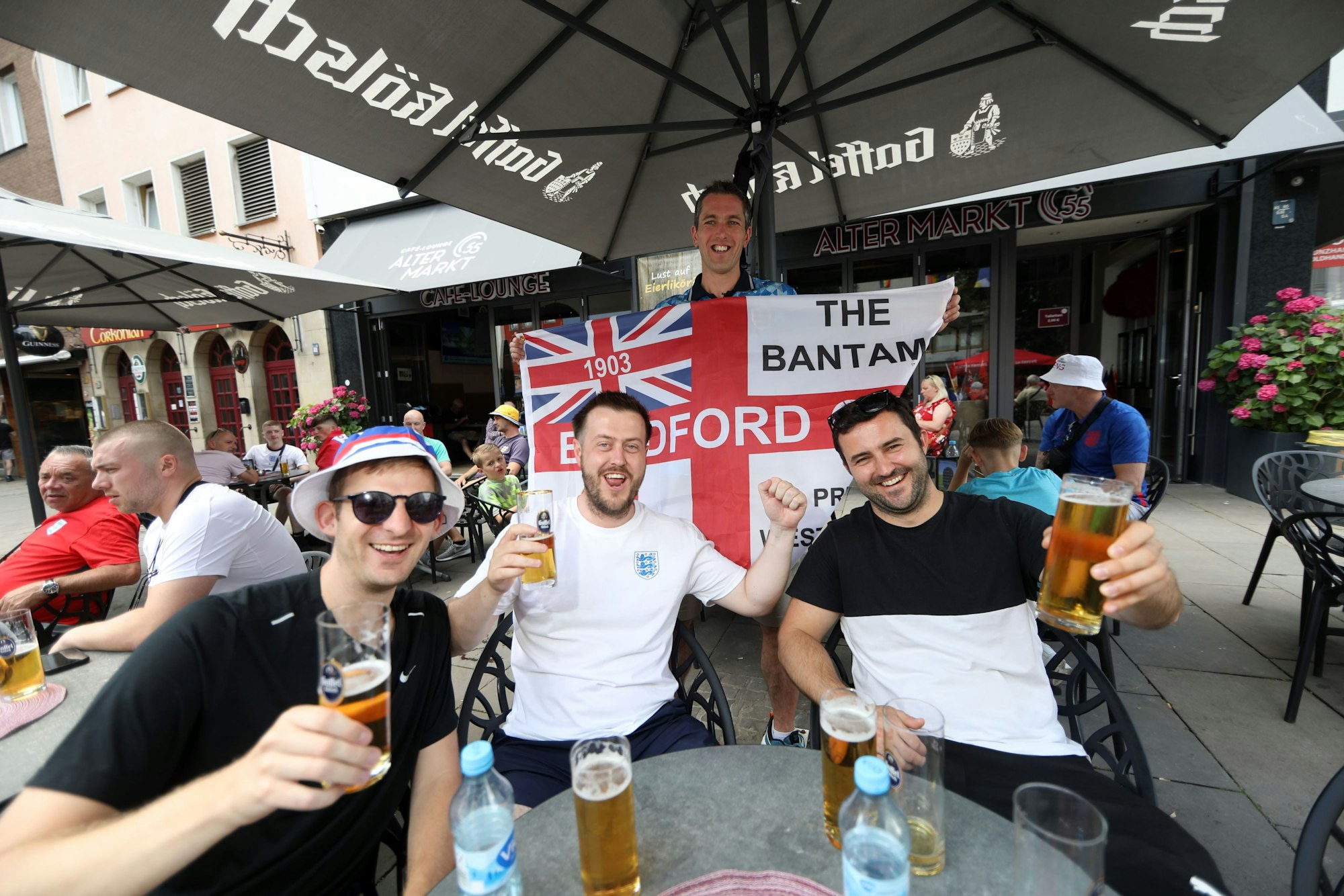 Englandfans sitzen am Alter Markt in einem Restaurant und prosten mit einem Glas Bier in die Kamera.