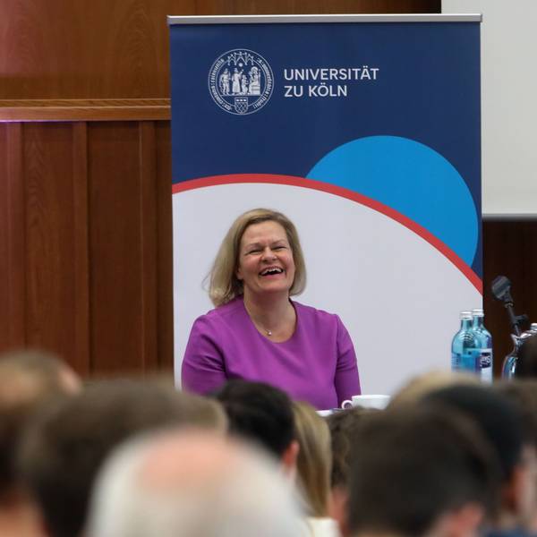 Bundesinnenministerin Nancy Faeser sitzt auf einem Podium in einem Hörsaal der Uni Köln.