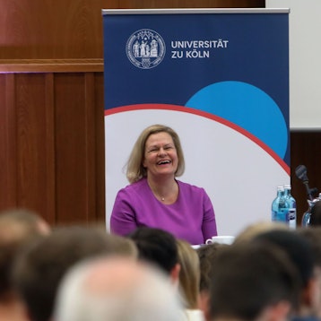 Bundesinnenministerin Nancy Faeser sitzt auf einem Podium in einem Hörsaal der Uni Köln.