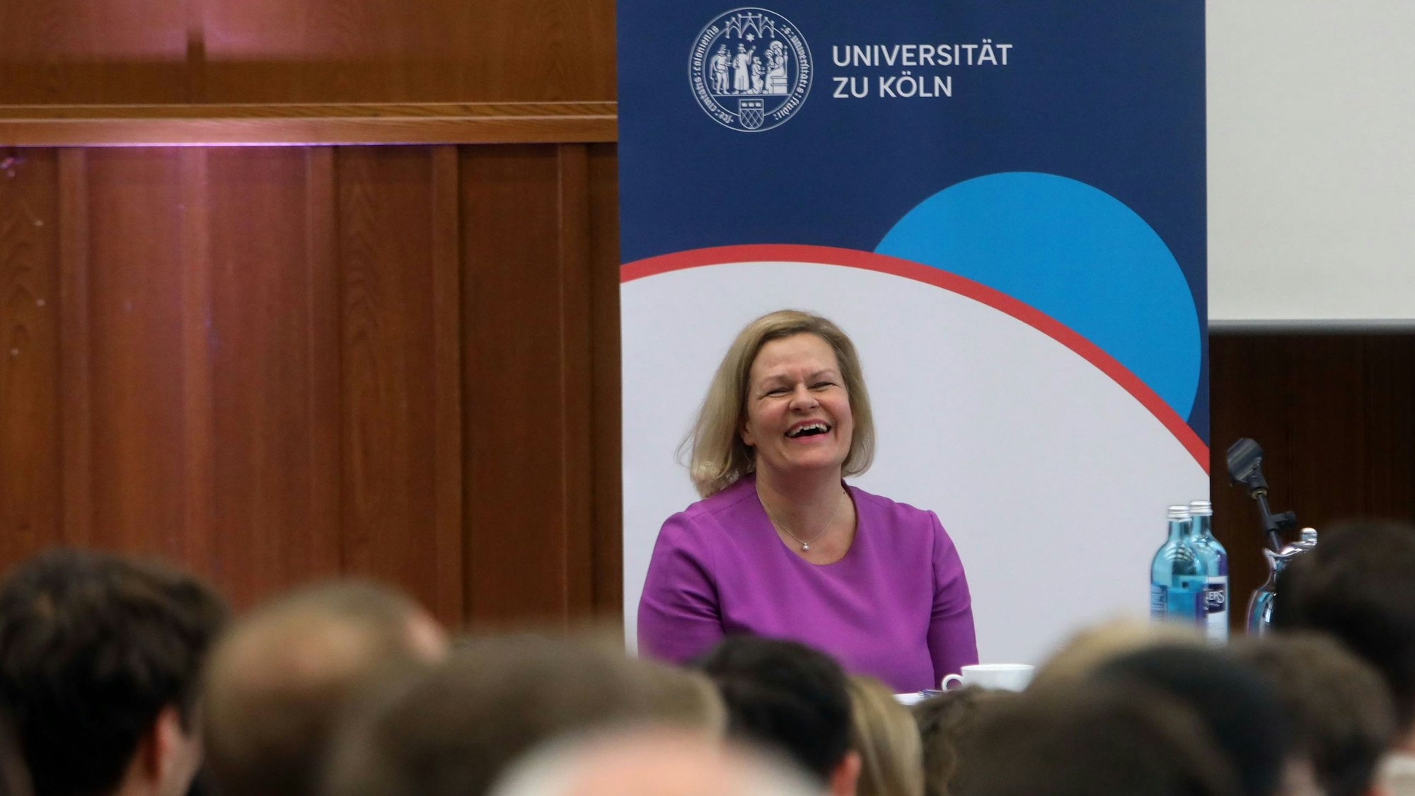 Bundesinnenministerin Nancy Faeser sitzt auf einem Podium in einem Hörsaal der Uni Köln.