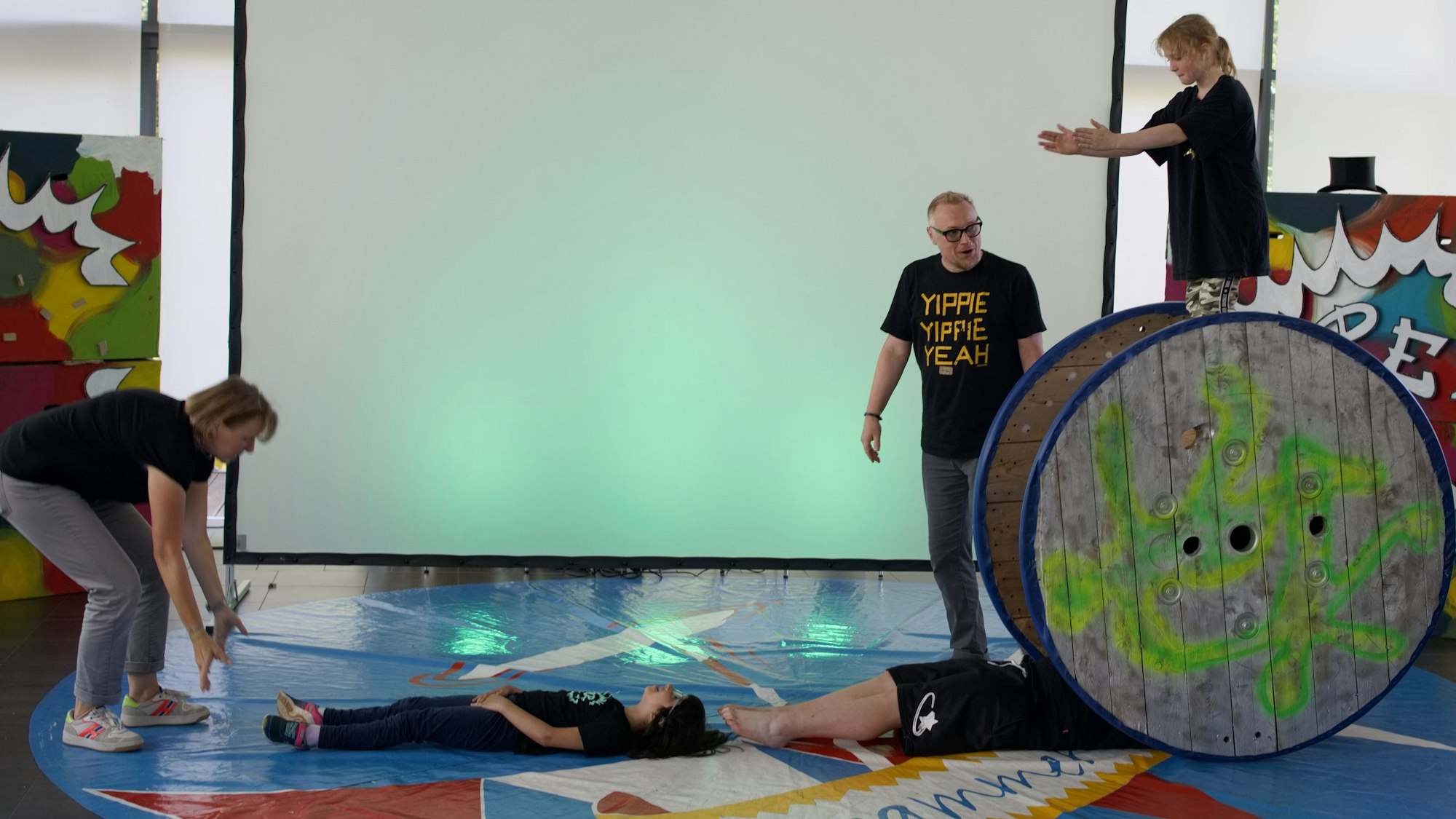 Ein Kind läuft auf einer Rolle, darunter liegen weitere Kinder flach auf dem Boden.