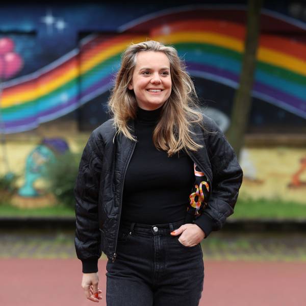 Ricarda Hofman steht vor einer Mauer auf die ein Regenbogen gemalt ist.