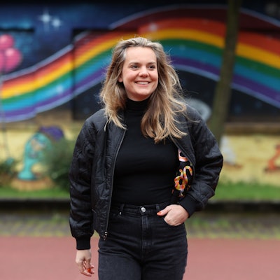 Ricarda Hofman steht vor einer Mauer auf die ein Regenbogen gemalt ist.