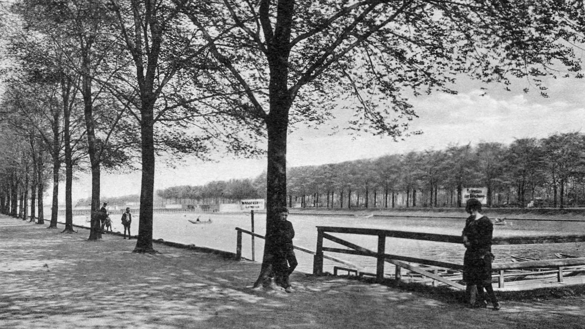Zu sehen ist ein Park mit einem Gewässer und ein paar Menschen.