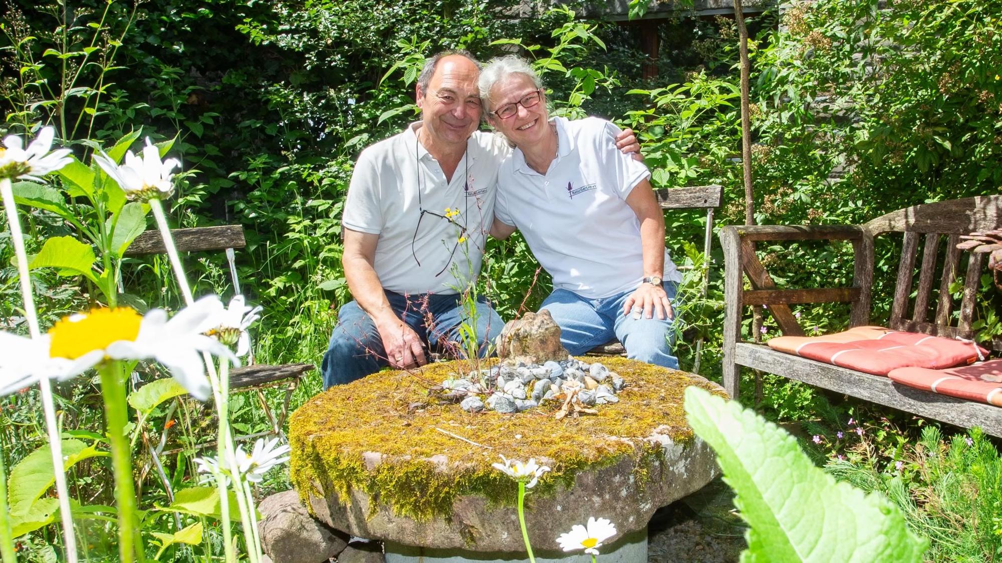 Ein Paar sitzt auf Gartenstühlen im Grünen und umarmt sich.