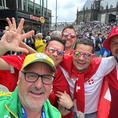 EM-Volunteer Mike Pütz in Köln mit vier jubelnden Fußballfans aus der Schweiz in rot-weißem Outfit.