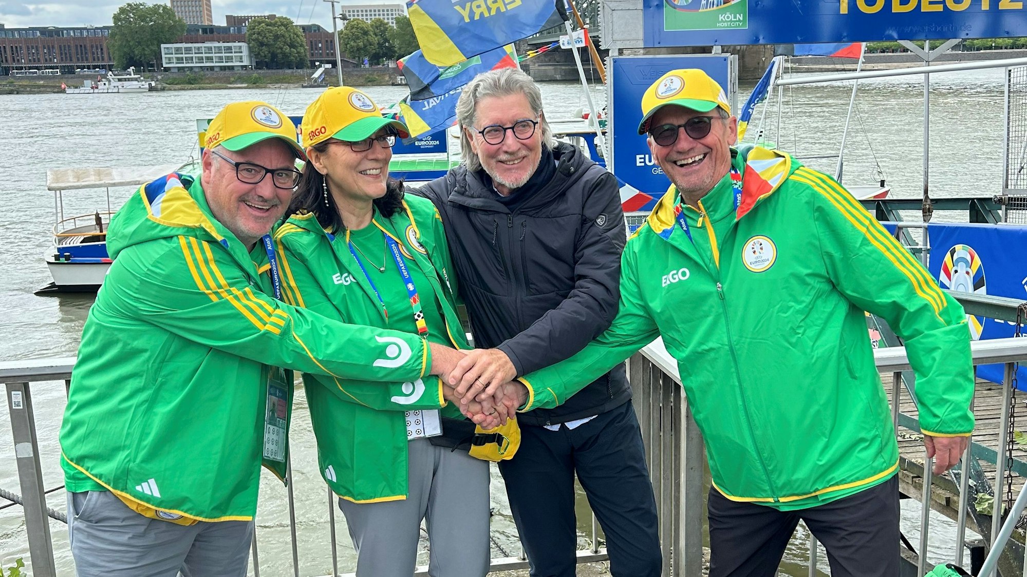 Vier Personen stehen am Rheinufer, es sind drei EM-Volunteere und der frühere Nationaltorhüter Toni Schumacher.