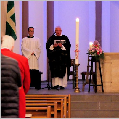 Ein Pfarrer steht am Altar von St. Nikolaus Bensberg, rechts ist neben Kerzen ein Bild des verstorbenen Heimatforschers Willi Fritzen zu sehen.