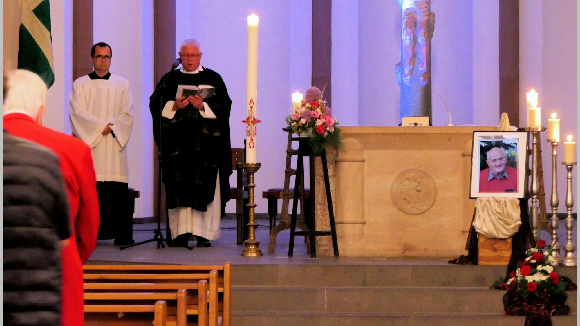 Ein Pfarrer steht am Altar von St. Nikolaus Bensberg, rechts ist neben Kerzen ein Bild des verstorbenen Heimatforschers Willi Fritzen zu sehen.