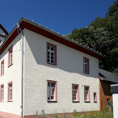 Im Vordergrund ist das Alte Pfarrhaus an der evangelischen Kirche in Hellenthal zu sehen, dahinter lugt der Kirchturm hervor.