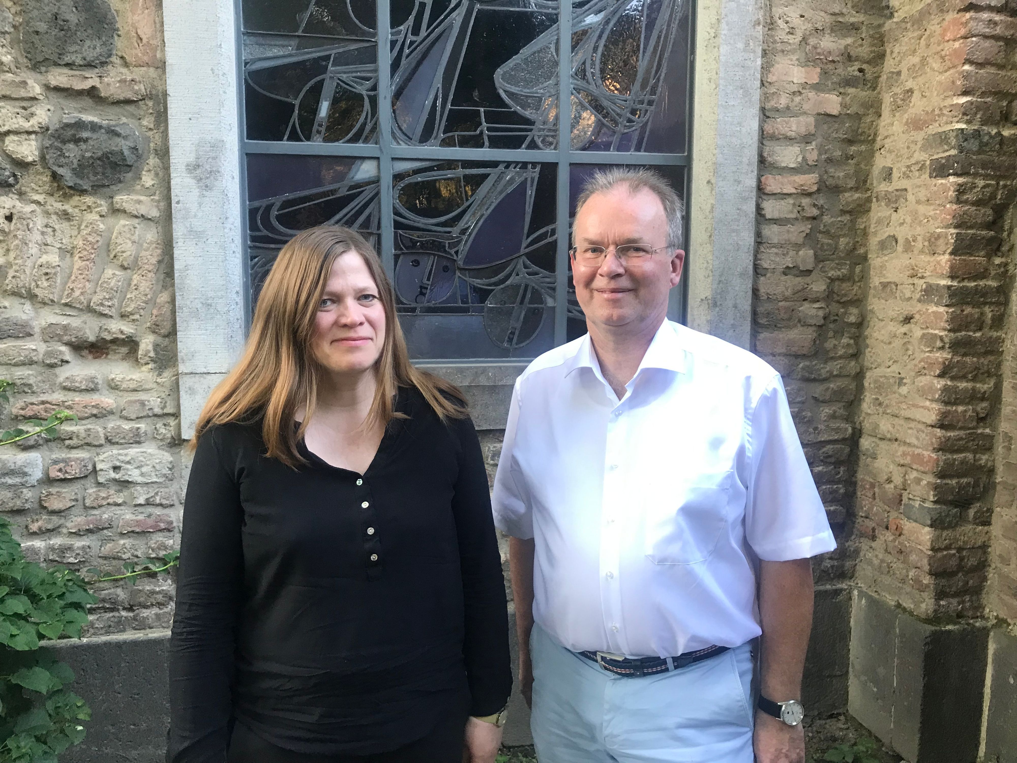 Eine Frau in schwarzem Oberteil und ein Mann in weißem Hemd vor einer Kirche