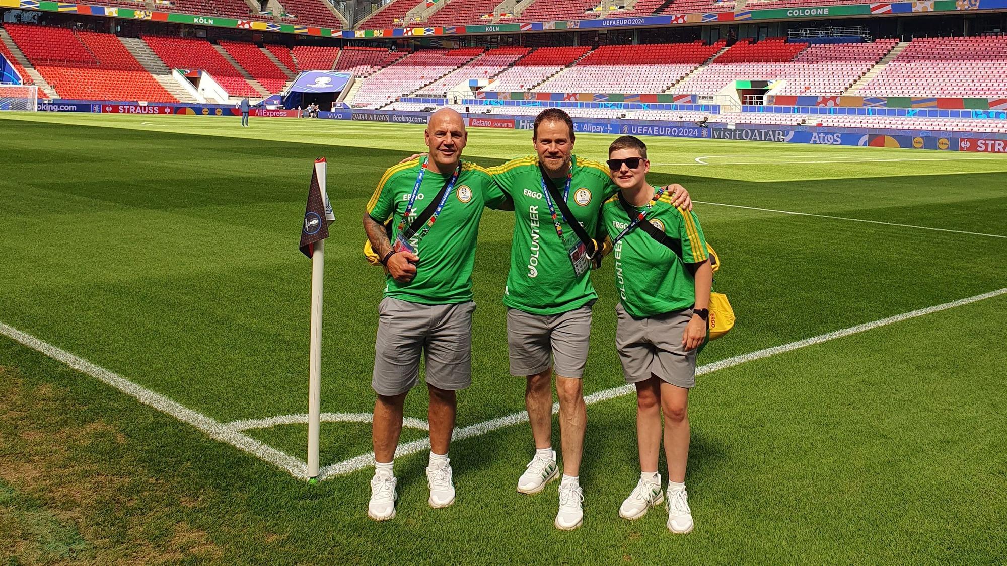 Die EM-Volunteers Roland Huppertz (Keldenich), Laurie Simon (Lorbach) und Jörg Piana (Kall) stehen im noch fast leeren Kölner Stadion an einer Eckfahne.