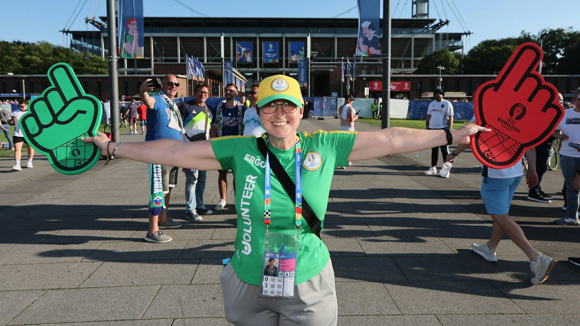 Volunteer Frauke Medri steht mit zwei Schaumstoffhänden vor dem Stadion in Köln