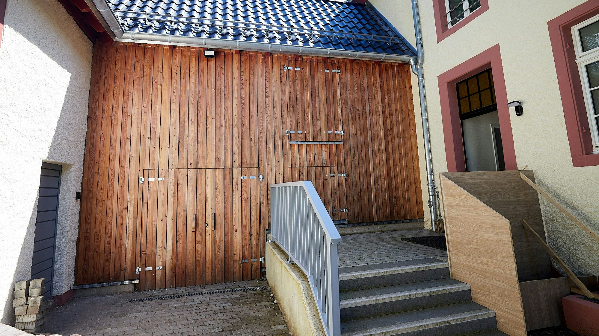 Mit Holz ist die Fassade eines kleinen Anbaus zwischen zwei Gebäuden verkleidet.