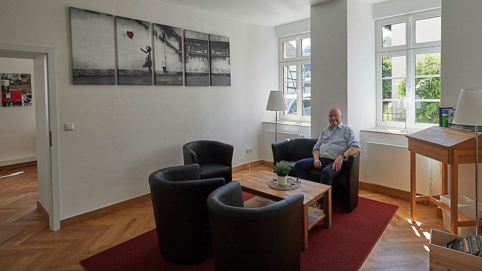 Pfarrer Oliver Joswig sitzt in einem Sessel einer Sitzgruppe in einem neu gestalteten Raum in Alten Pfarrhaus in Hellenthal.