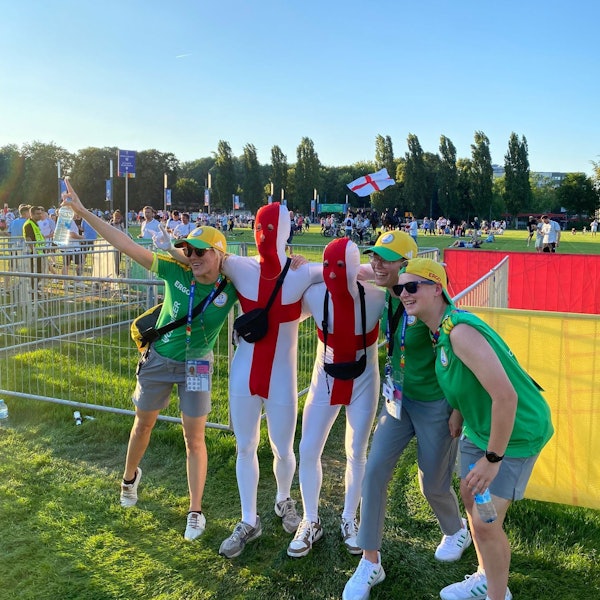 Laurie Simon und zwei weitere EM-Volunteers posieren mit Fans, die rot-weiße Ganzkörperanzüge tragen.