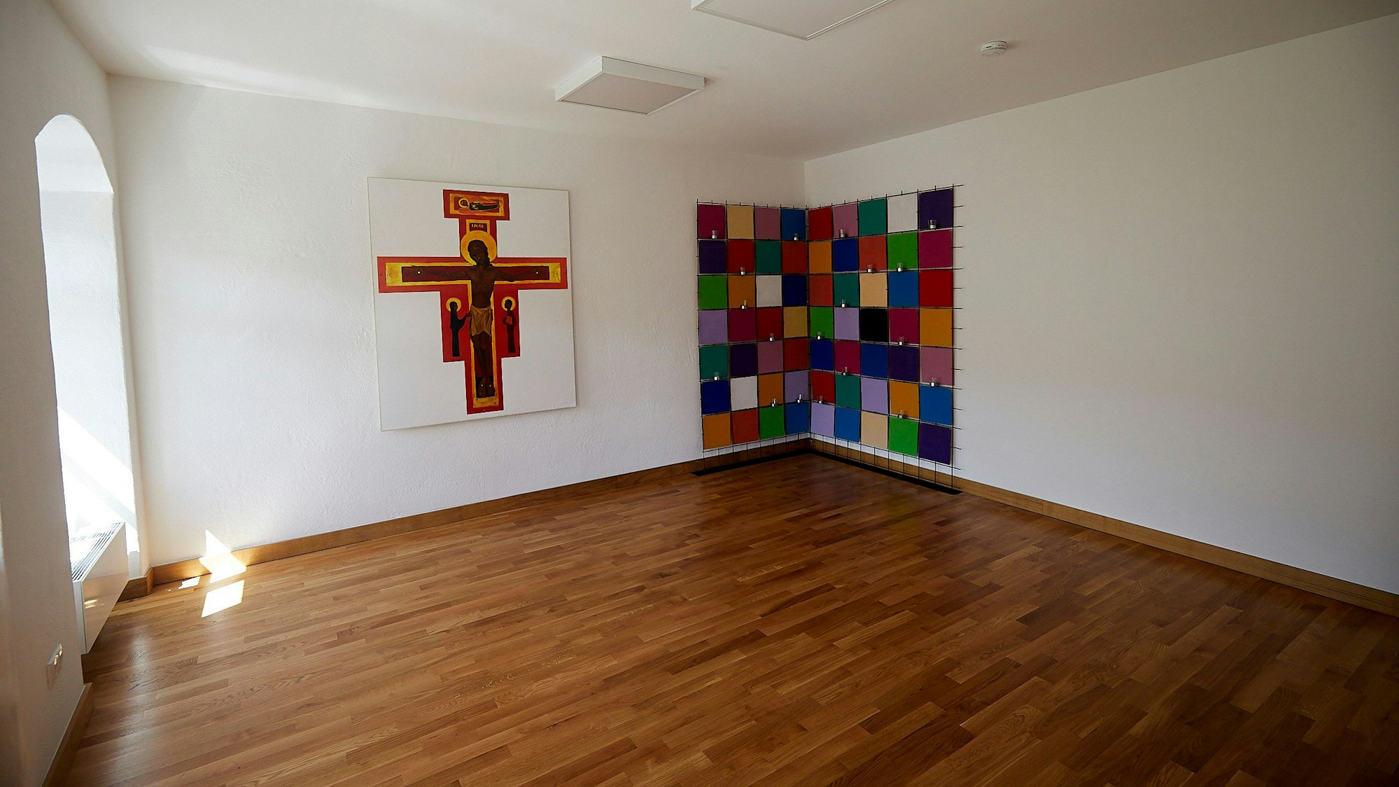 Im Alten Pfarrhaus in Hellenthal wird ein Raum für Taizé-Gebete genutzt. Der Raum ist leer, an der Wand hängen die bildliche Darstellung eines Kreuzes und ein vielfarbiges Bild.