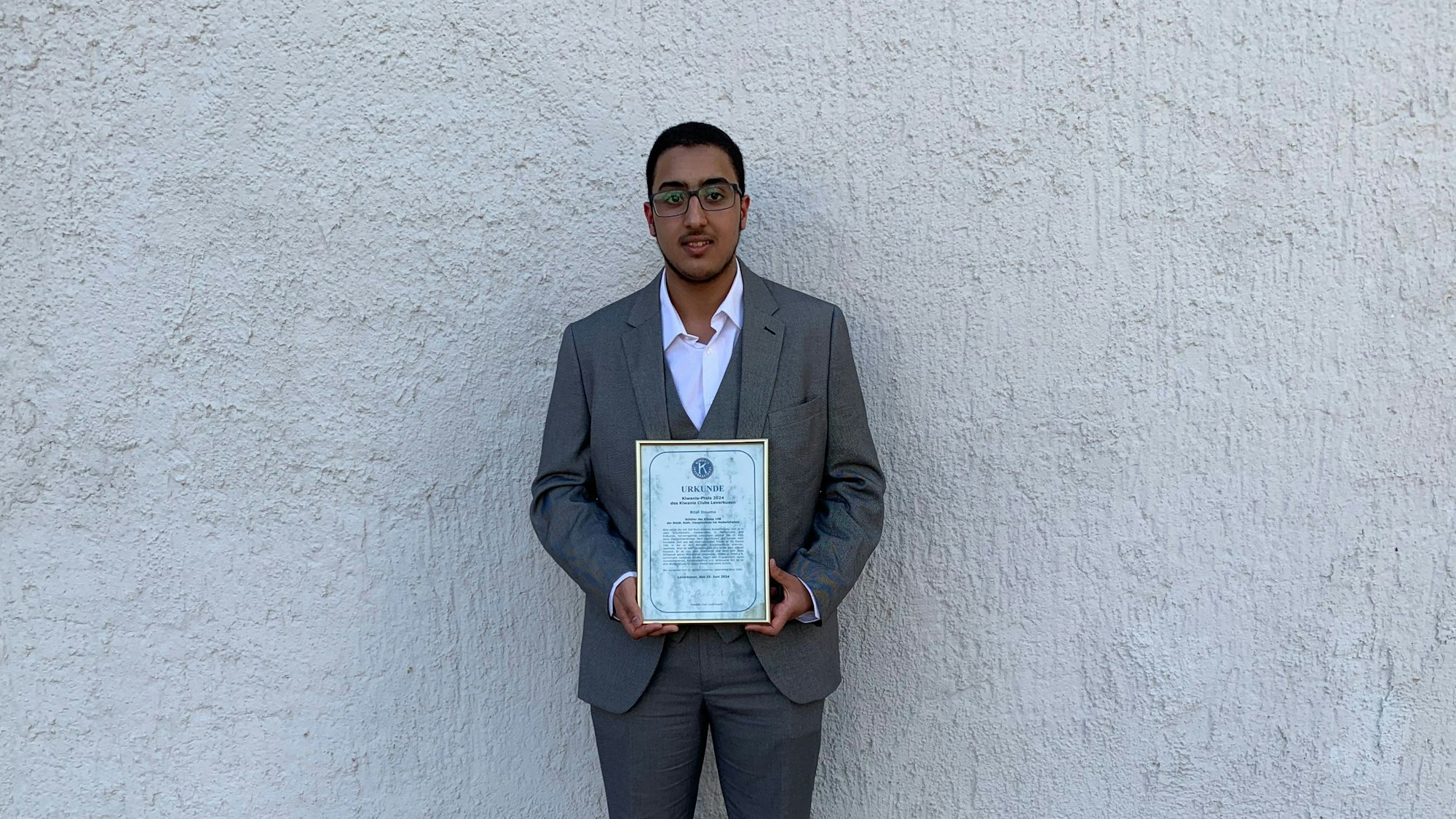 Ein Junge steht vor einer Wand und hält eine Urkunde.