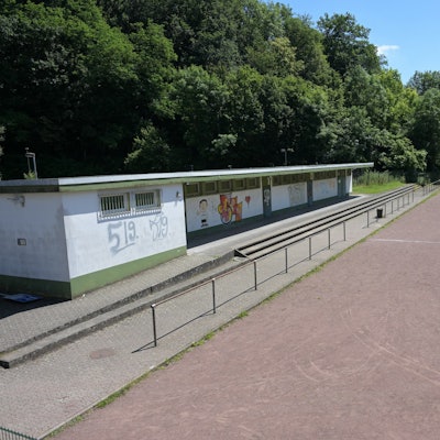 Ein Sportplatz mit Fußballrasen, auf dem ein Tor steht, eine Aschenbahn und etwas unansehnliche Umkleiden.