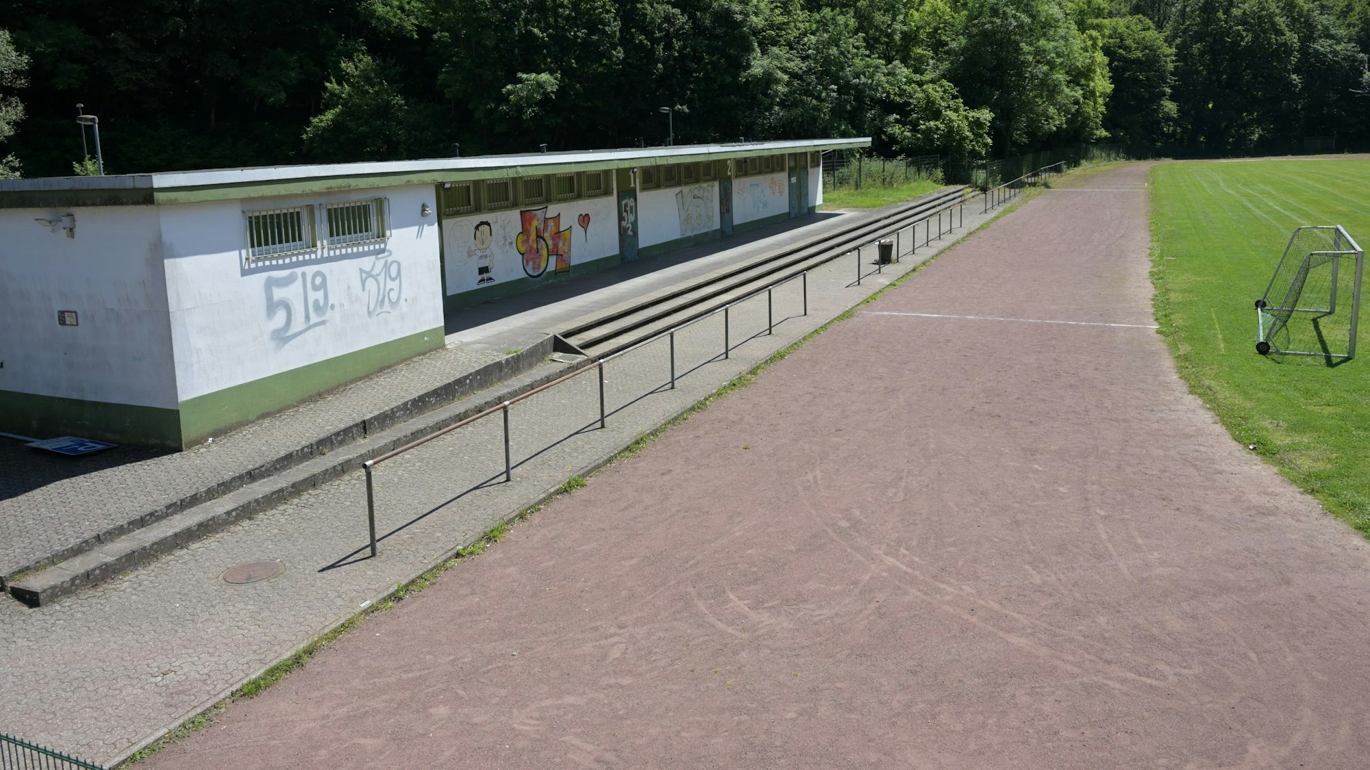 Ein Sportplatz mit Fußballrasen, auf dem ein Tor steht, eine Aschenbahn und etwas unansehnliche Umkleiden.