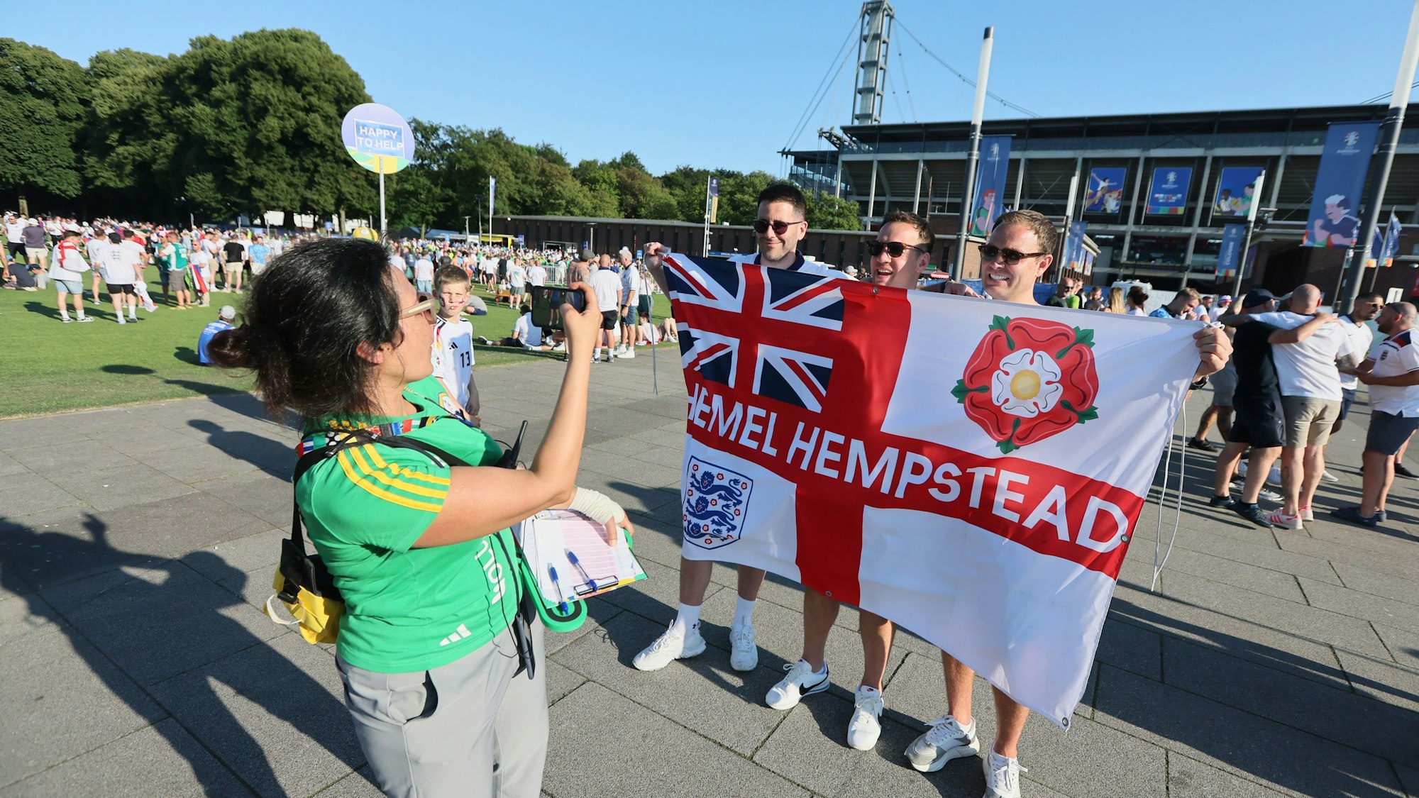 EM-Volunteer Sophia Papageorgiou fotografiert drei englische Fans mit einer Fahne vor dem Kölner Stadion