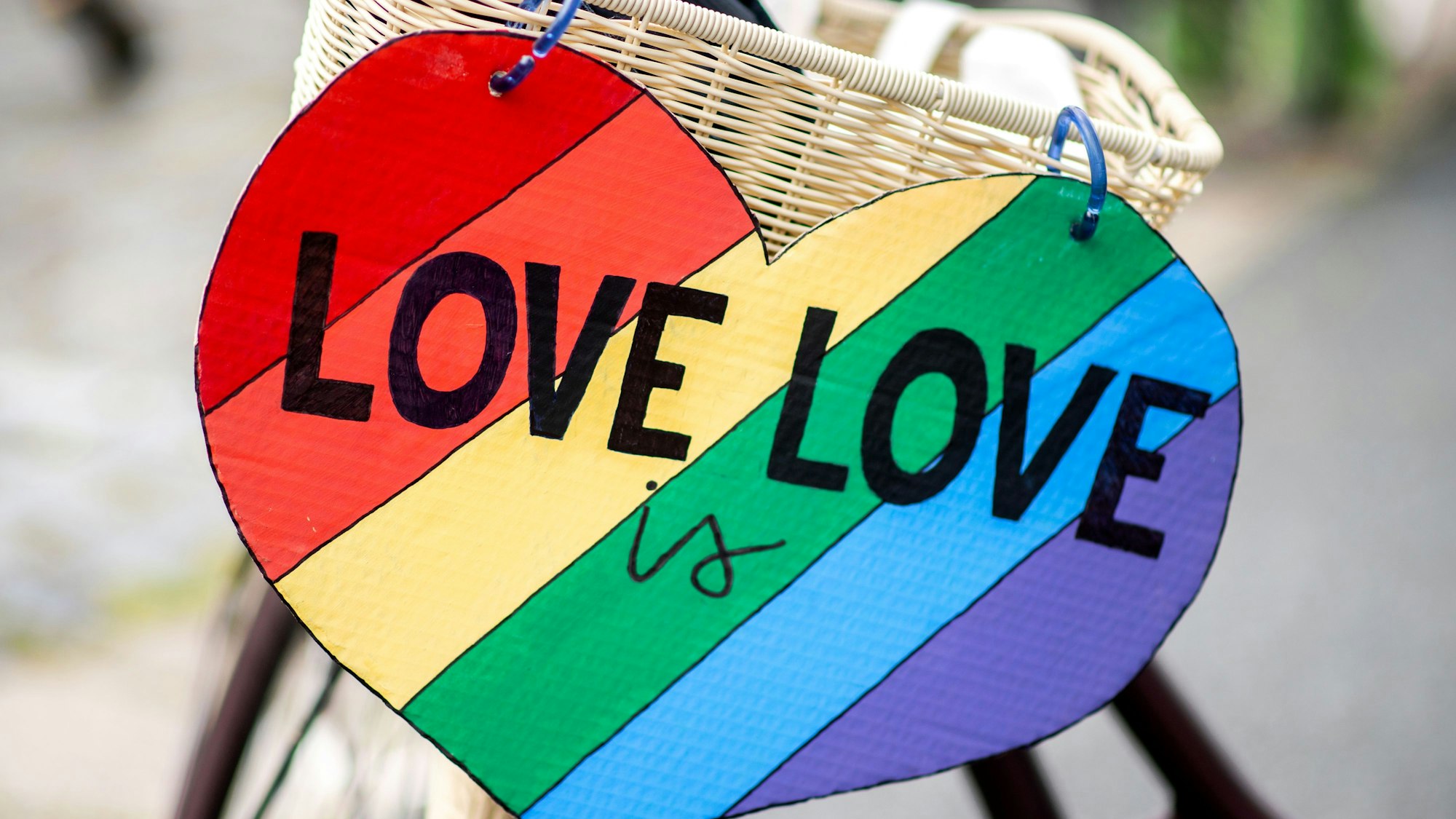 Ein herzförmiges Schild mit der Aufschrift "Love is Love" hängt im Rahmen des CSD (Christopher Street Day) am Fahrrad einer Teilnehmerin.