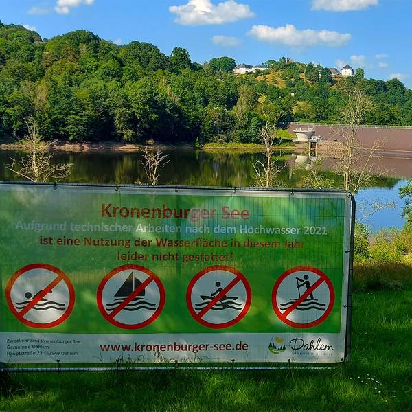 Vor dem Kronenburger See ist ein Schild aufgestellt. Die Aufschrift lautet: „Aufgrund technischer Arbeiten nach dem Hochwasser 2021 ist eine Nutzung der Wasserfläche in diesem Jahr leider nicht gestattet!“
