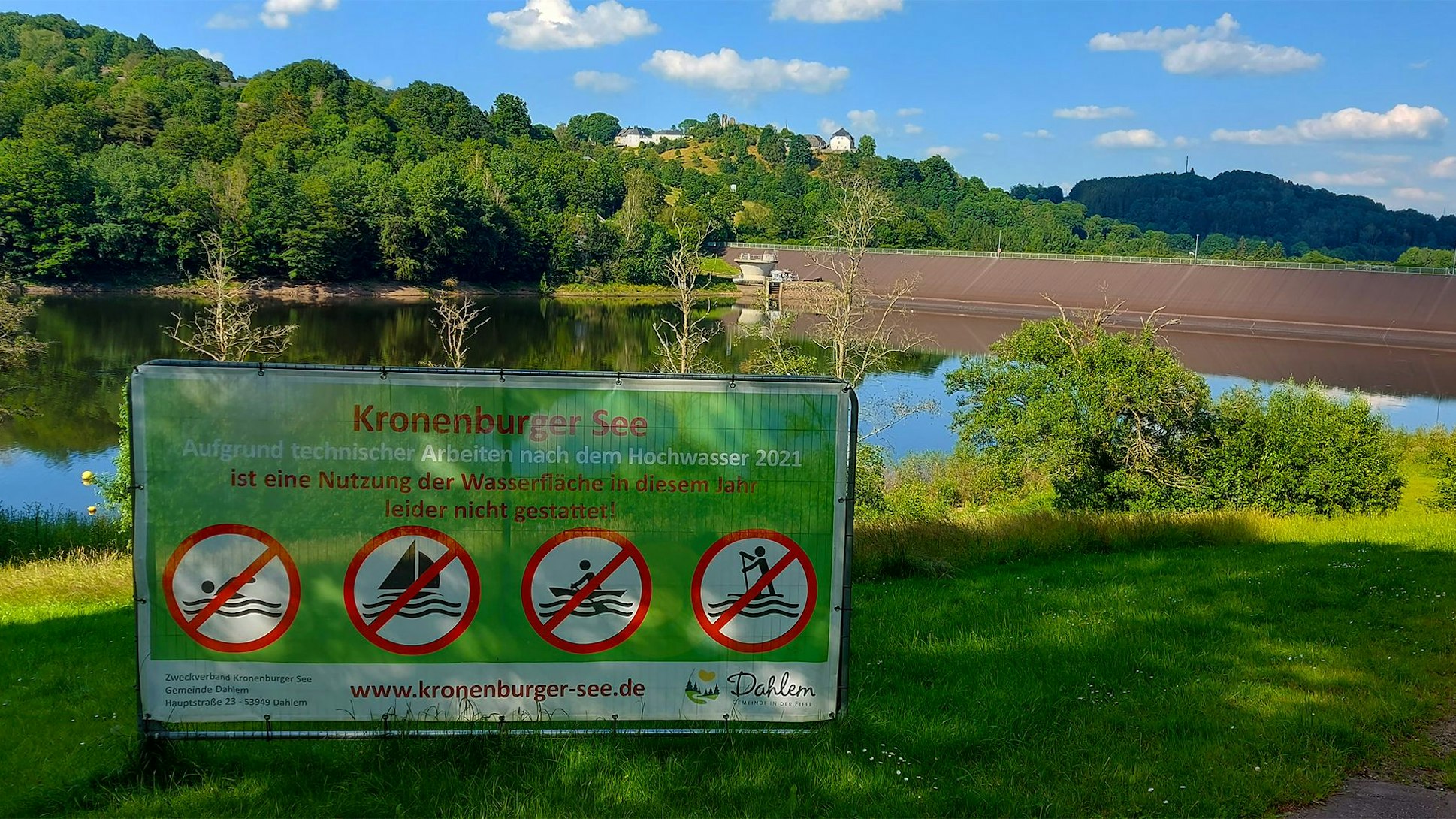 Vor dem Kronenburger See ist ein Schild aufgestellt. Die Aufschrift lautet: „Aufgrund technischer Arbeiten nach dem Hochwasser 2021 ist eine Nutzung der Wasserfläche in diesem Jahr leider nicht gestattet!“