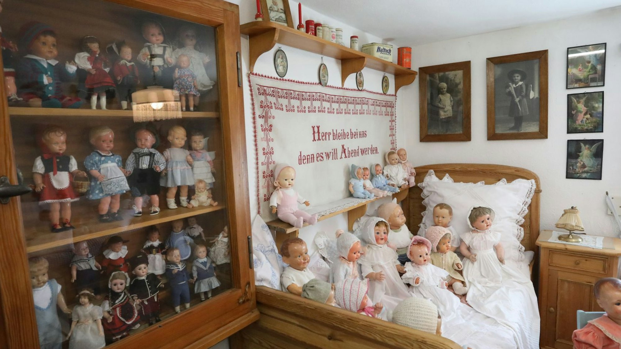 Viele Puppen stehen in einer Vitrine und liegen auf einem alten Bauernbett.