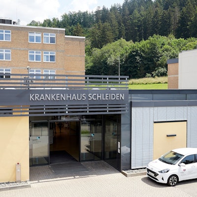 Das Bild zeigt den Haupteingang des Krankenhauses Schleiden, davor parkt ein Auto.