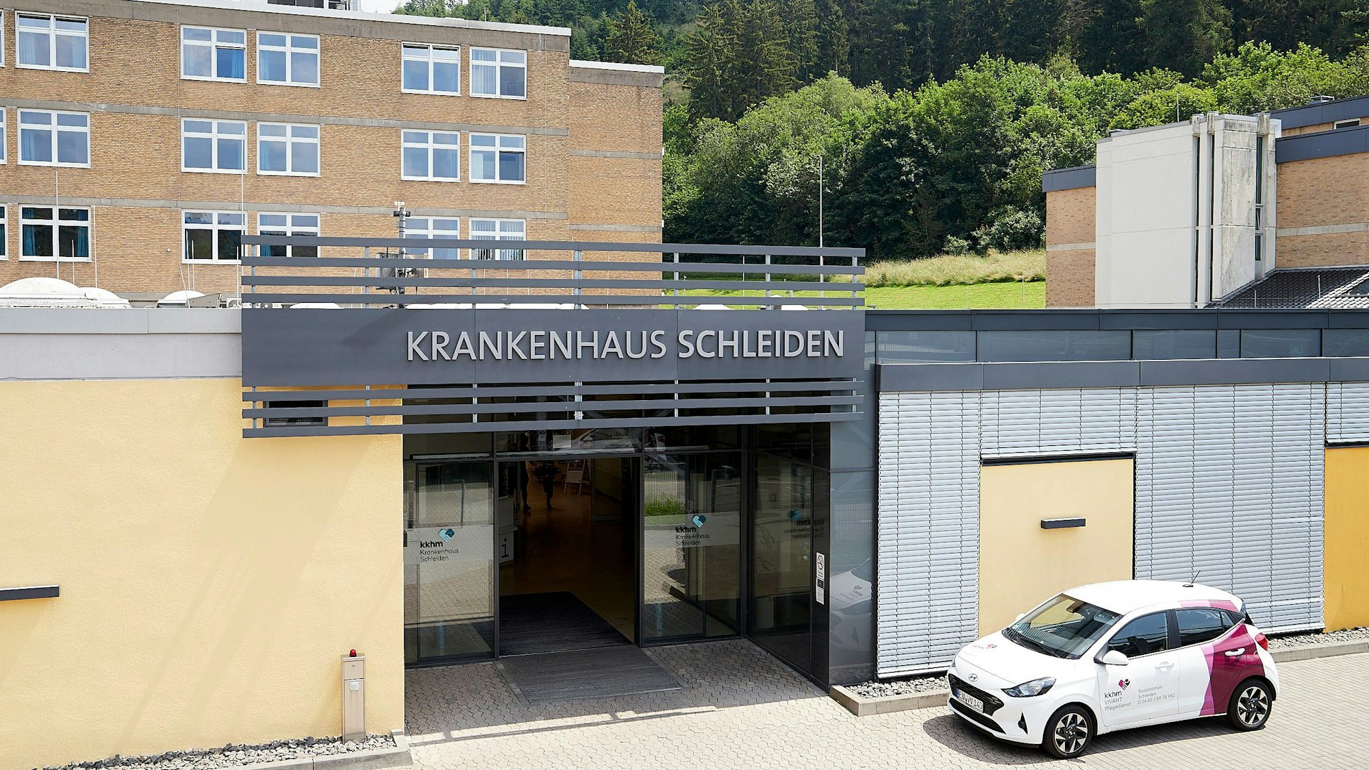 Das Bild zeigt den Haupteingang des Krankenhauses Schleiden, davor parkt ein Auto.