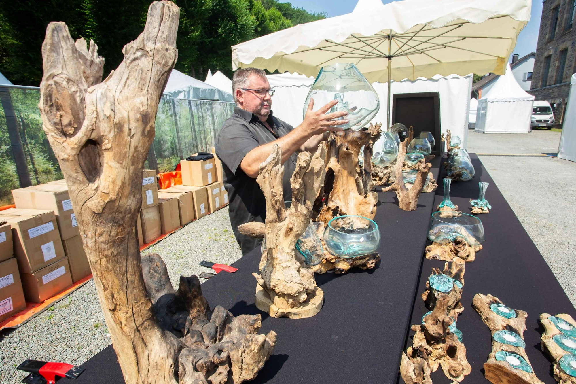 Ein Man drapiert eine große Glasschale in einer geschnitzten Wurzel, im Hintergrund sind weitere Pavillons zu erkennen.