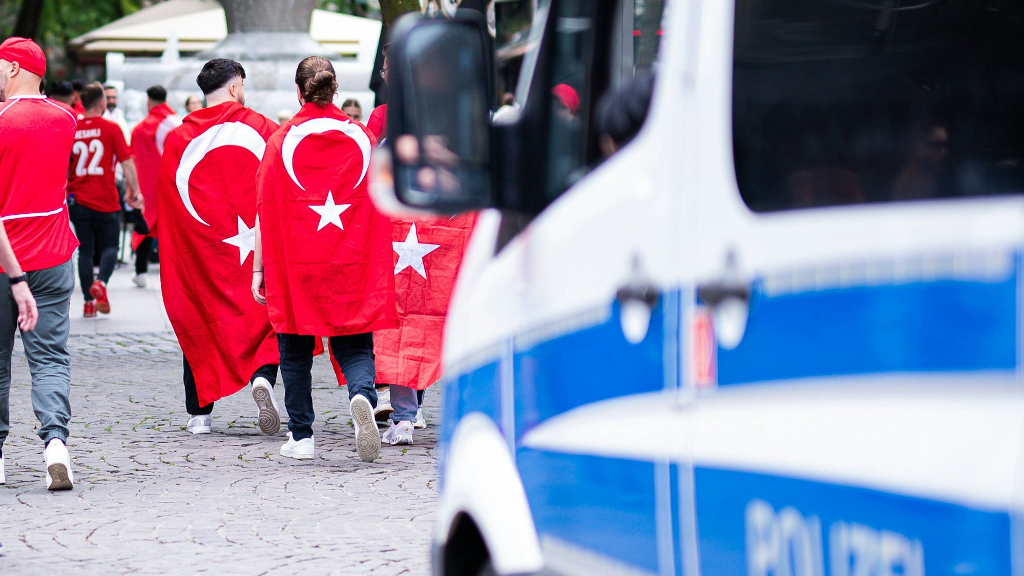 Türkische Fans gehen an einem Polizeiauto vorbei.