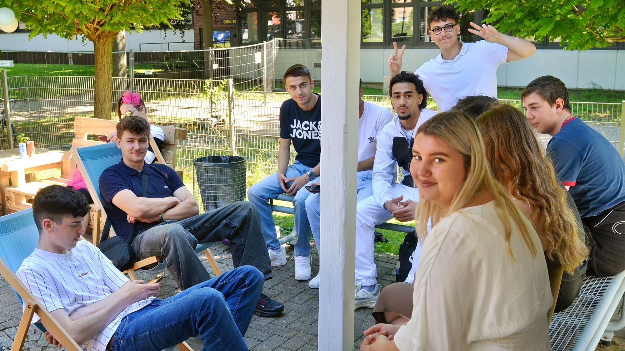 Schülerinnen und Schüler des Thomas-Eßer-Berufskollegs sitzen im Freien zusammen und blicken in die Kamera.