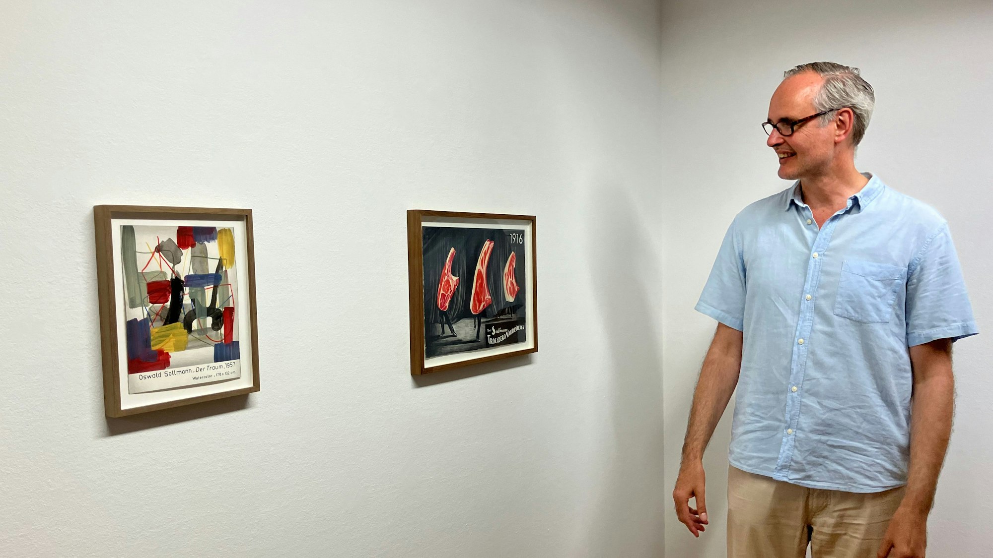 Kurator Fritz Emslander steht vor zwei kleinformatigen Zeichnungen van Eedens, darunter das Motiv der tanzenden Koteletts.