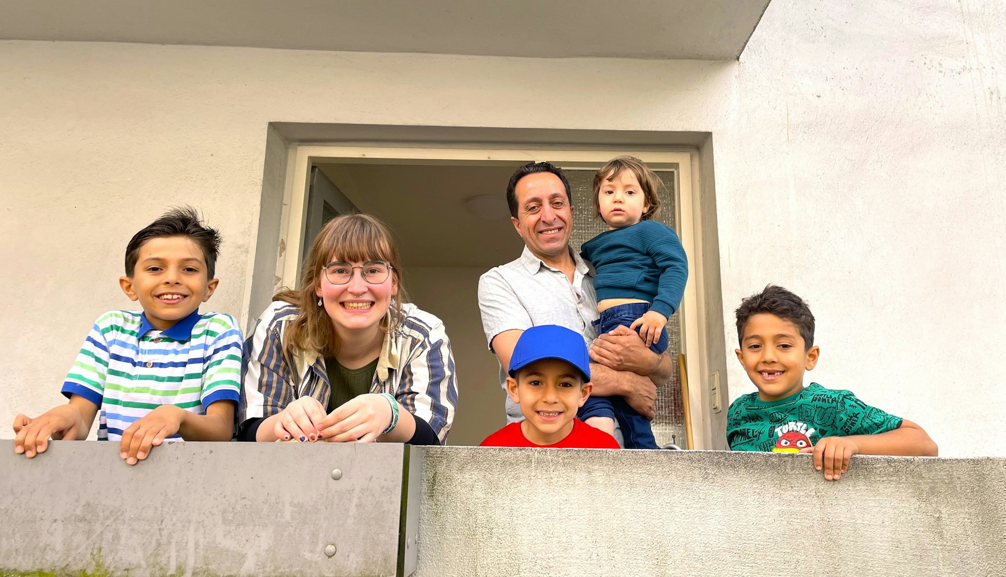 Jusef, 10, seine „KöKiPat“-Patin Kaja Niemann, seine kleinen Brüder und Vater Abdljafur Aldakhawi (von links) stehen auf dem betonierten Balkon ihrer Wohnung in Köln-Höhenhaus