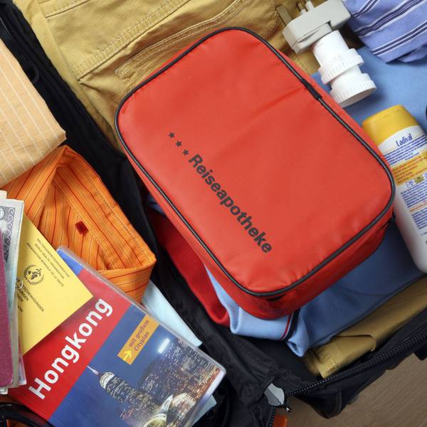 Auf einem gepackten, geöffneten Koffer liegt ein Medizin-Täschchen mit der Aufschrift Reiseapotheke